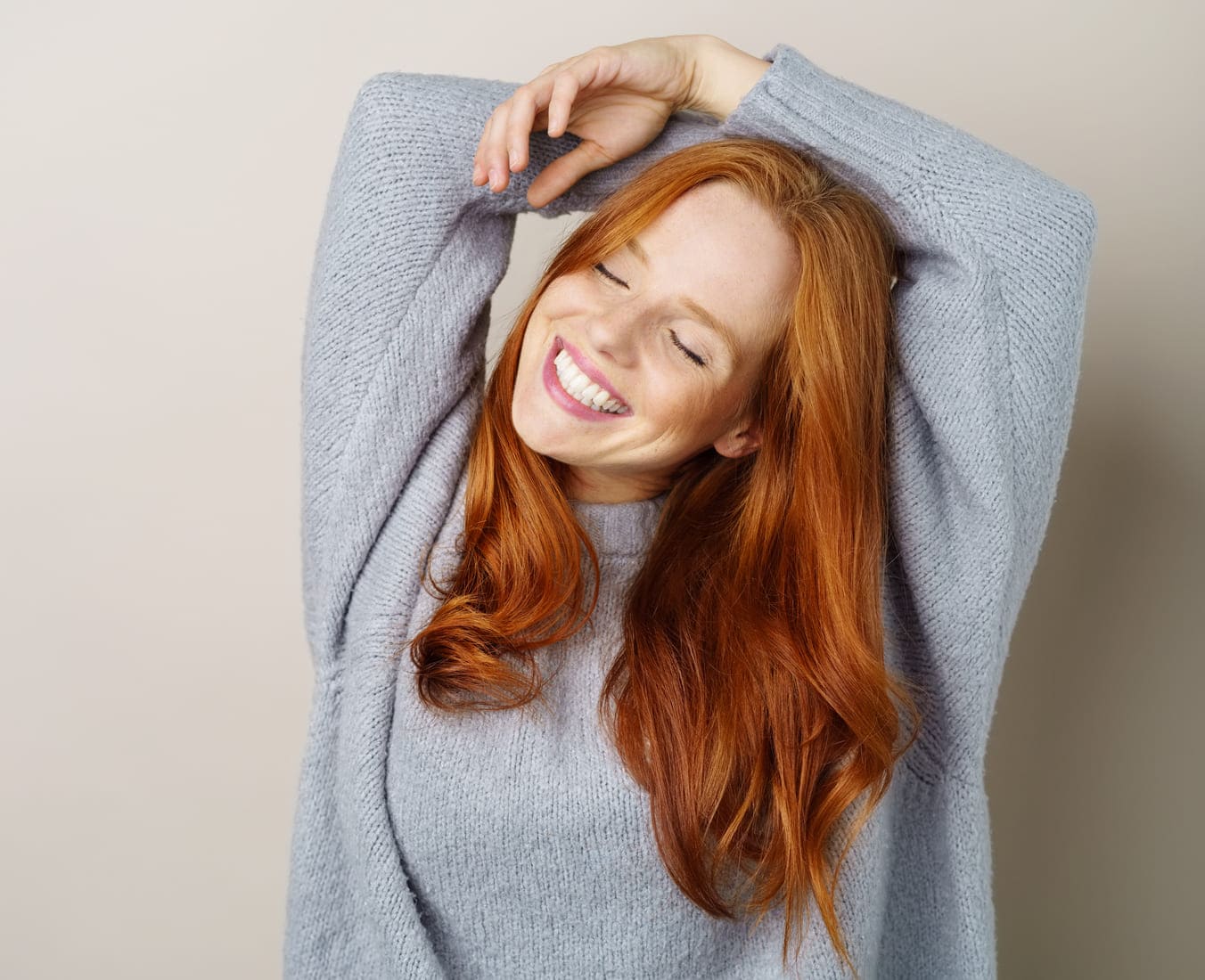 Jeune femme aux cheveux longs souriant, les bras levés au-dessus de sa tête