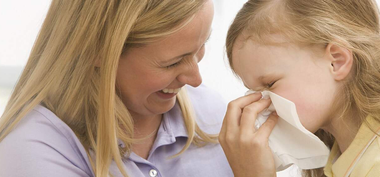 Mother helping daughter blow her nose and handle cold symptoms with MOTRIN®