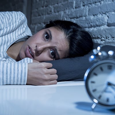 Femme couchée dans son lit, les yeux ouverts, l'horloge affichant les premières heures du matin