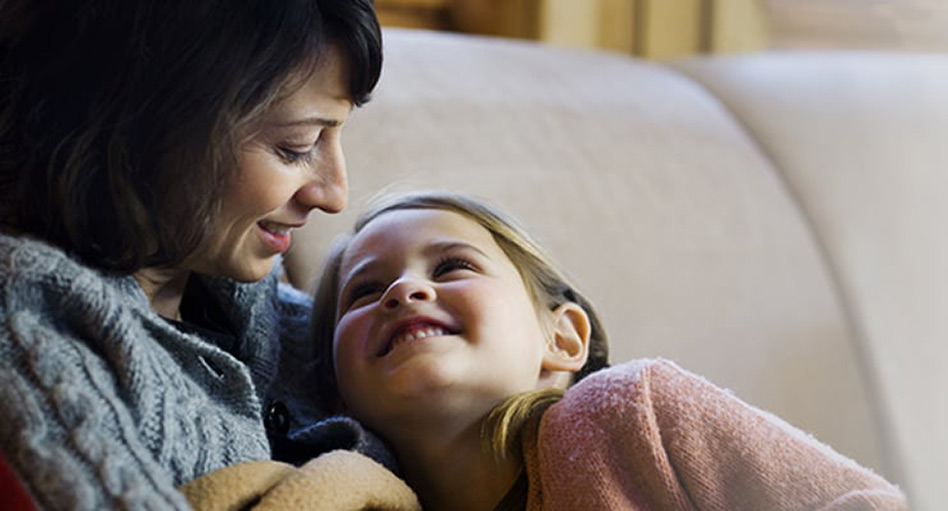 Mom smiling at her daughter while they sit on a couch