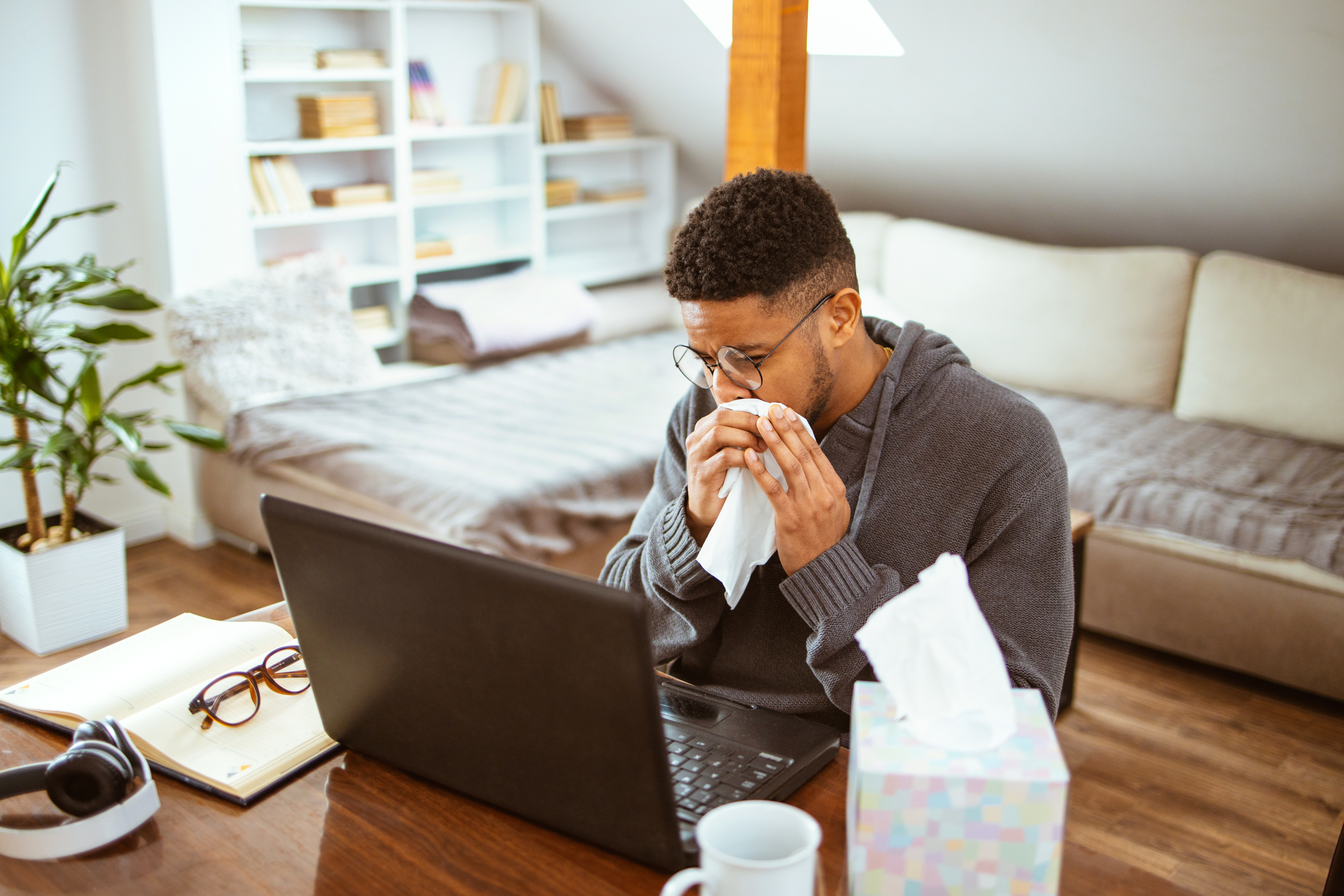 Man sneezing while working on a laptop at home.