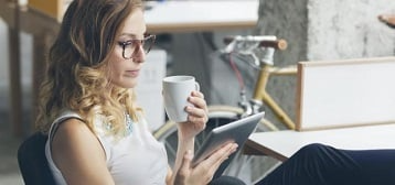 Woman holding a cup and reading on a tablet