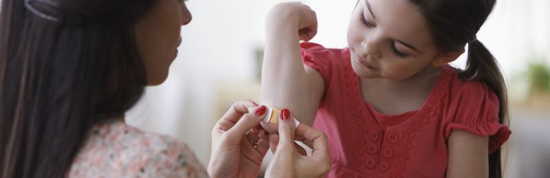 Woman putting a bandaid on a girl's elbow