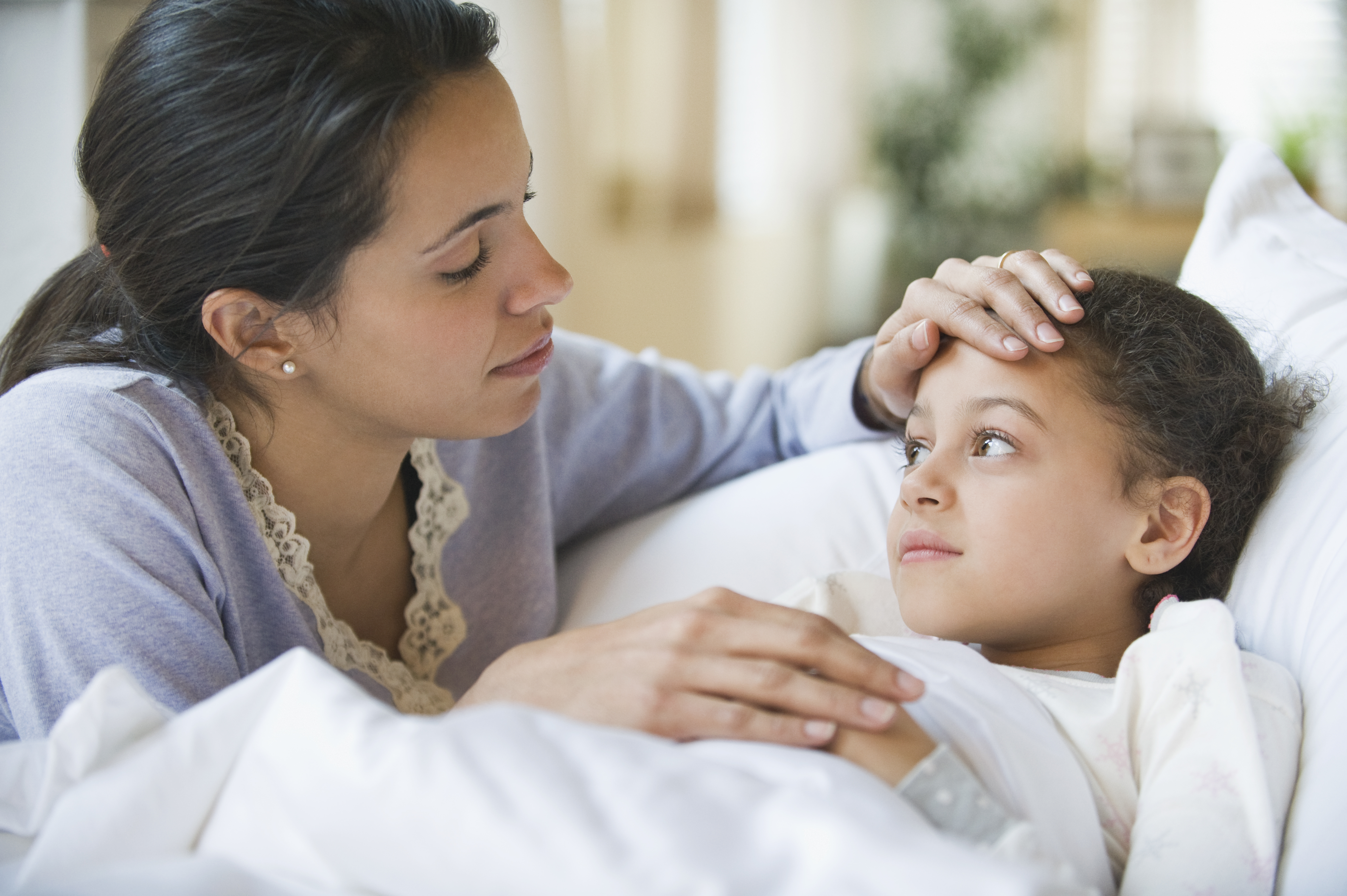 Woman checking temperature of her little ill daughter, who is lying in bed