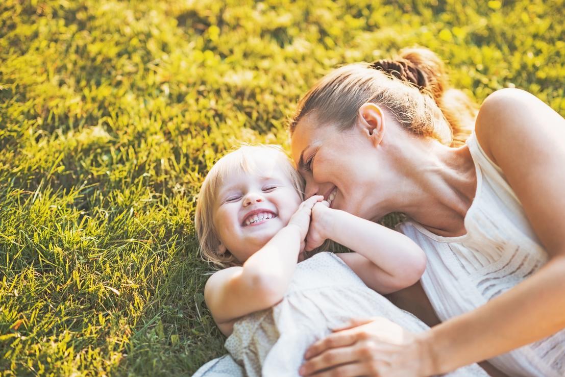 Mother and her young daughter lying on the grass and smiling.