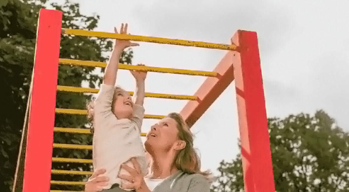 Woman helping her daughter reach the monkey bars