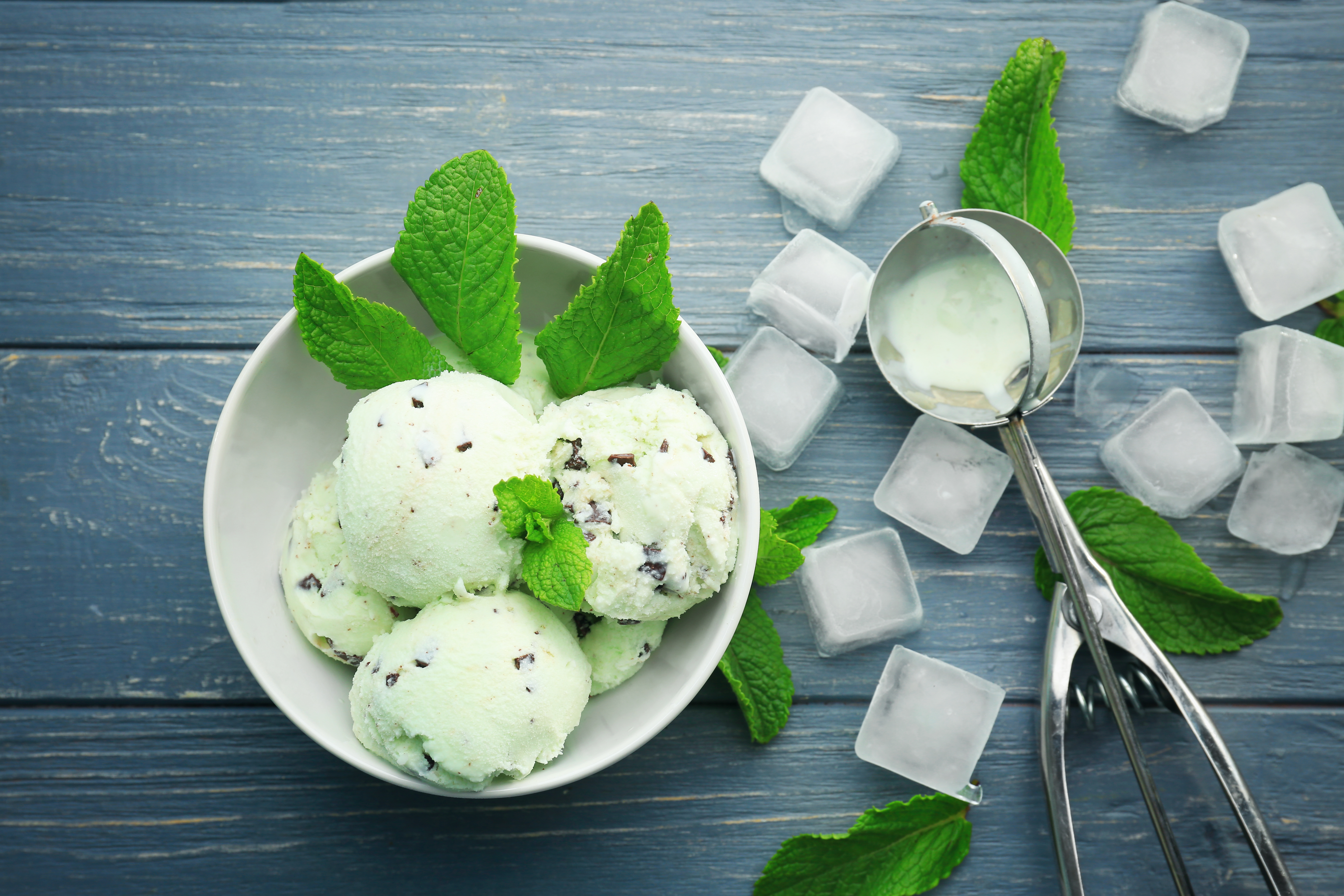 Quatre boules de crème glacée dans un bol avec des feuilles de menthe et des cubes de glace sur une table