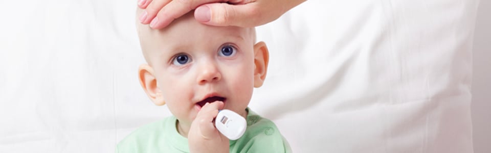 Infant holding a thermometer while mom checks his temperature