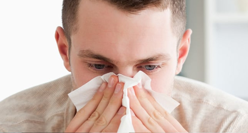 Young man with a beige sweater sitting on a cough blowing his nose