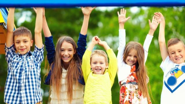 Five kids happily raising their hands in an outdoor playground