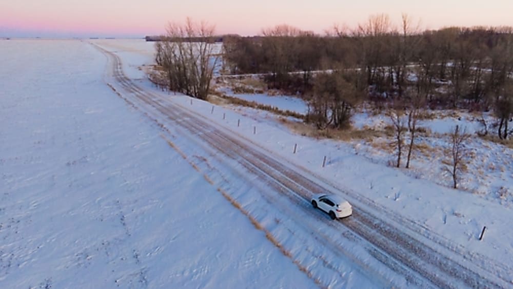 White SUV driving down a snow covered road in winter