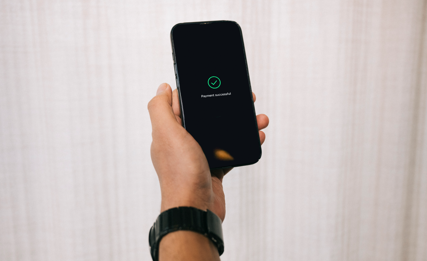 This image depicts a person's hand holding a phone which displays a confirmation screen saying 'Payment successful'.