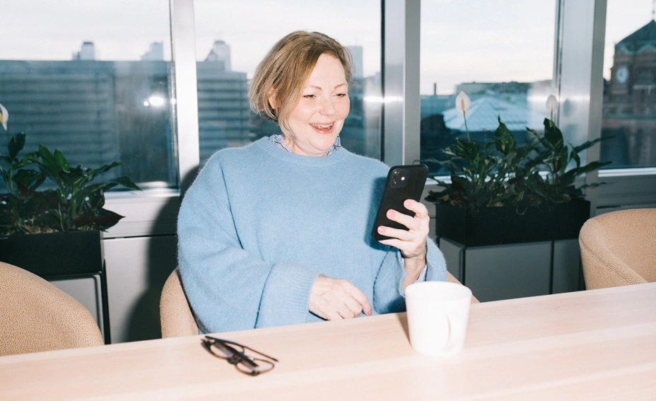 A woman holding up a mobile phone, looking at it and smiling