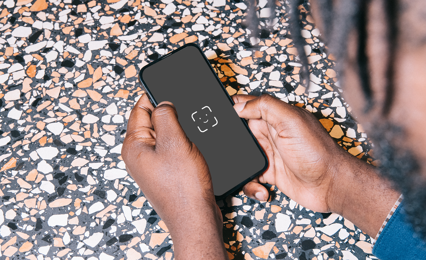 A person's hands looking at a mobile phone from above, which displays a face recognition screen.