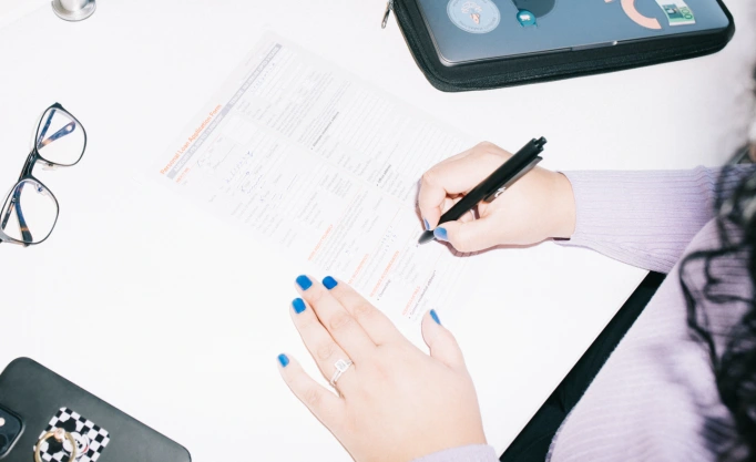 This image depicts a person’s hand from above, filling in a loan application form.