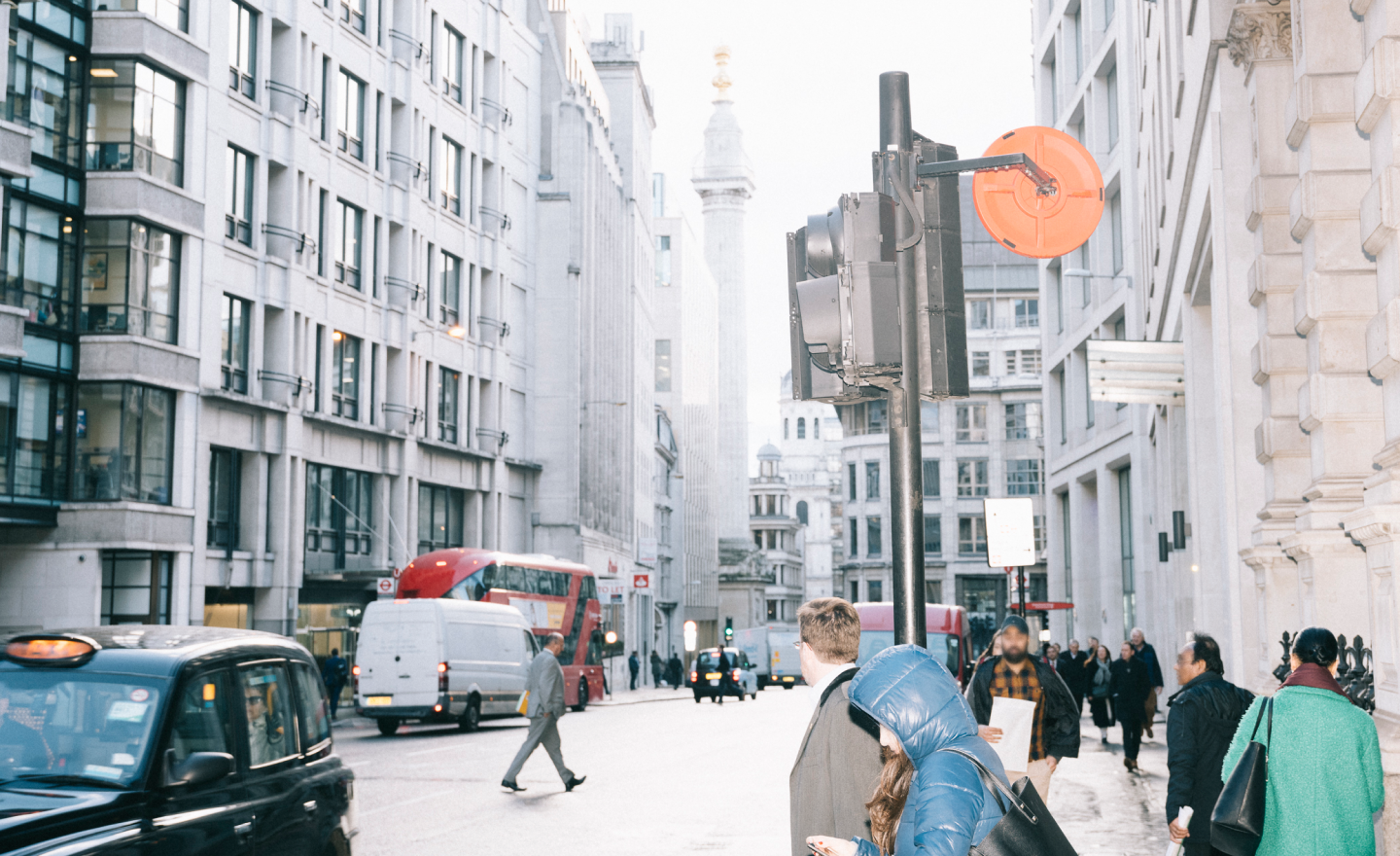 People on a streetscape with vehicles and buildings in the background.