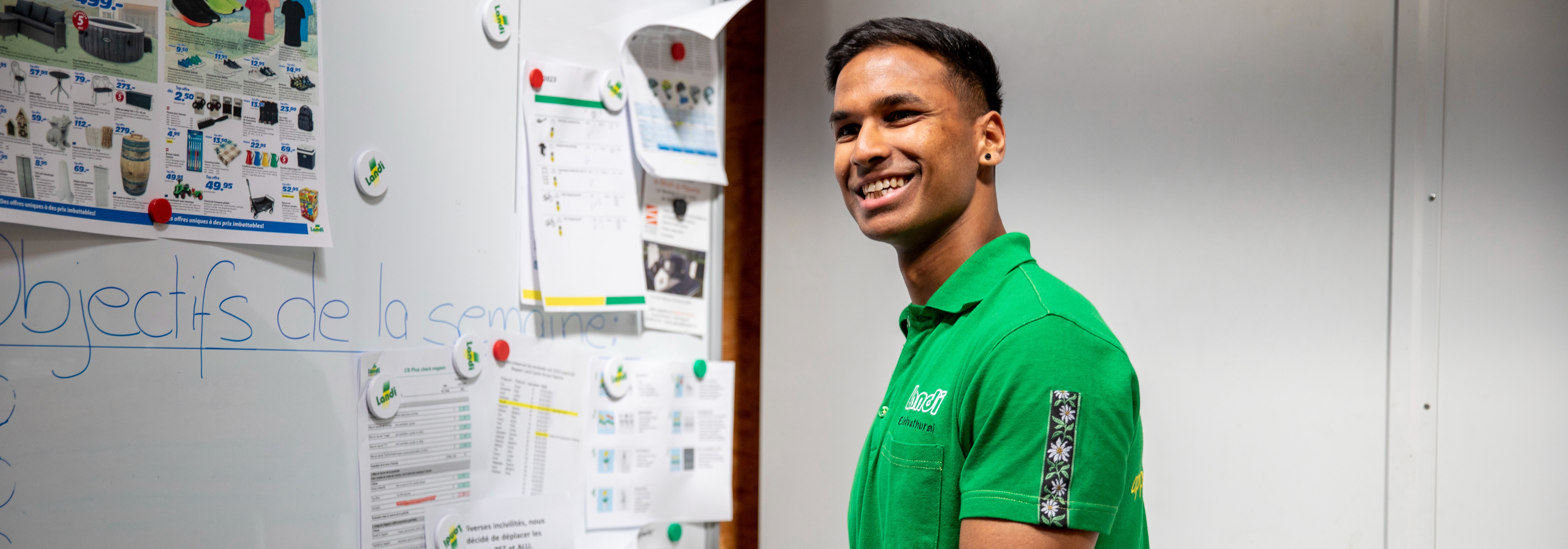 Hero, LANDI Centre-Broye, Mitarbeiter vor Plangungstafel mit Blick zur Kamera