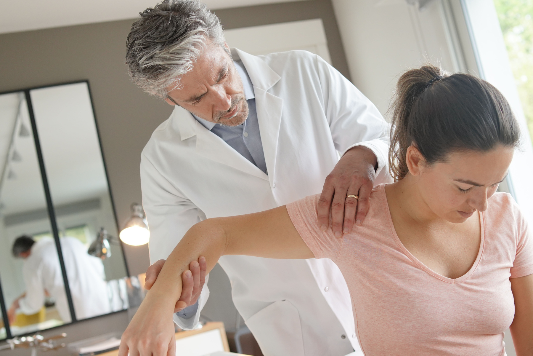 Doctor checking pain in shoulder for female patient