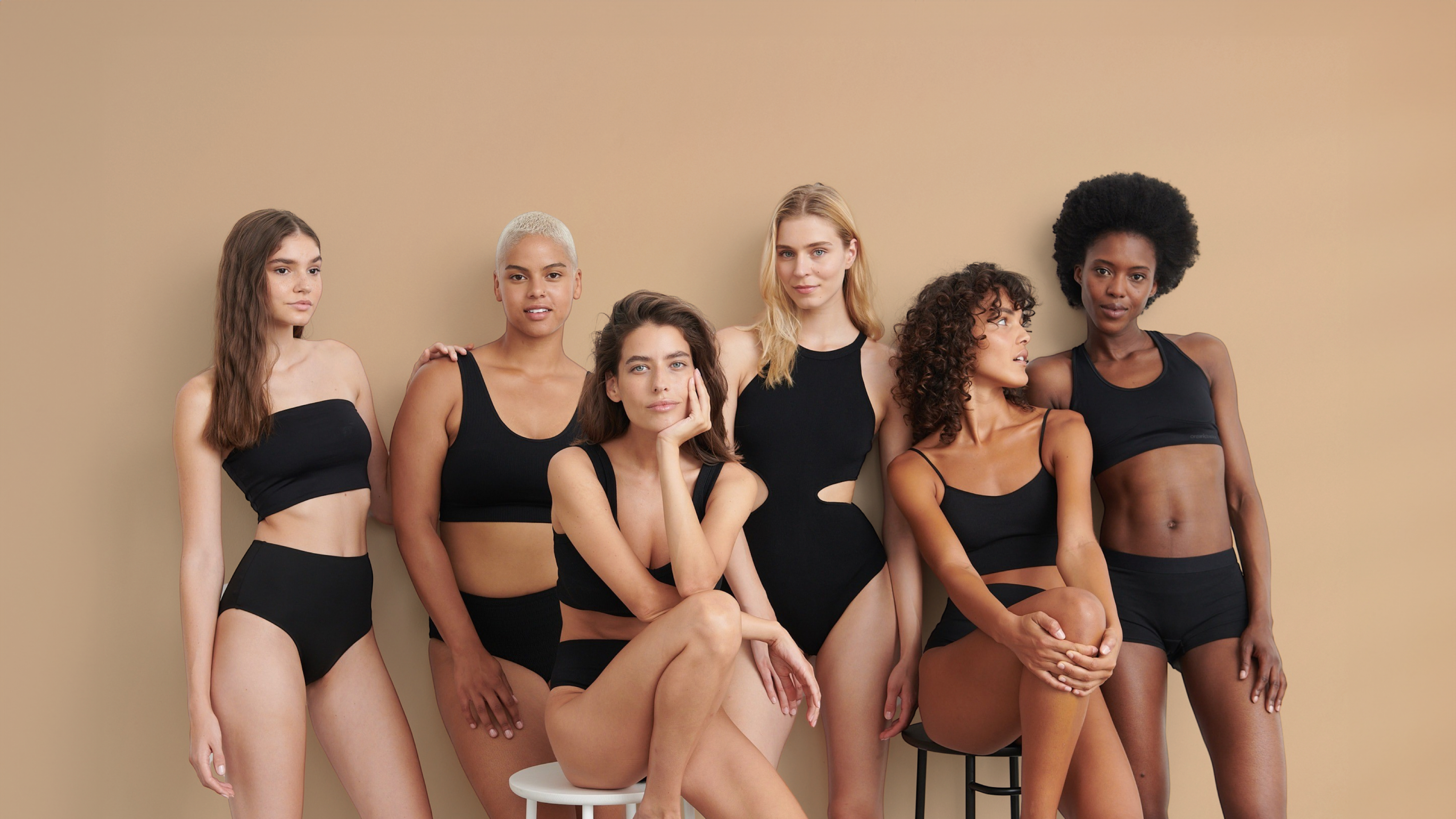 Group of 6 women in black sporty bikinis sitting and standing.