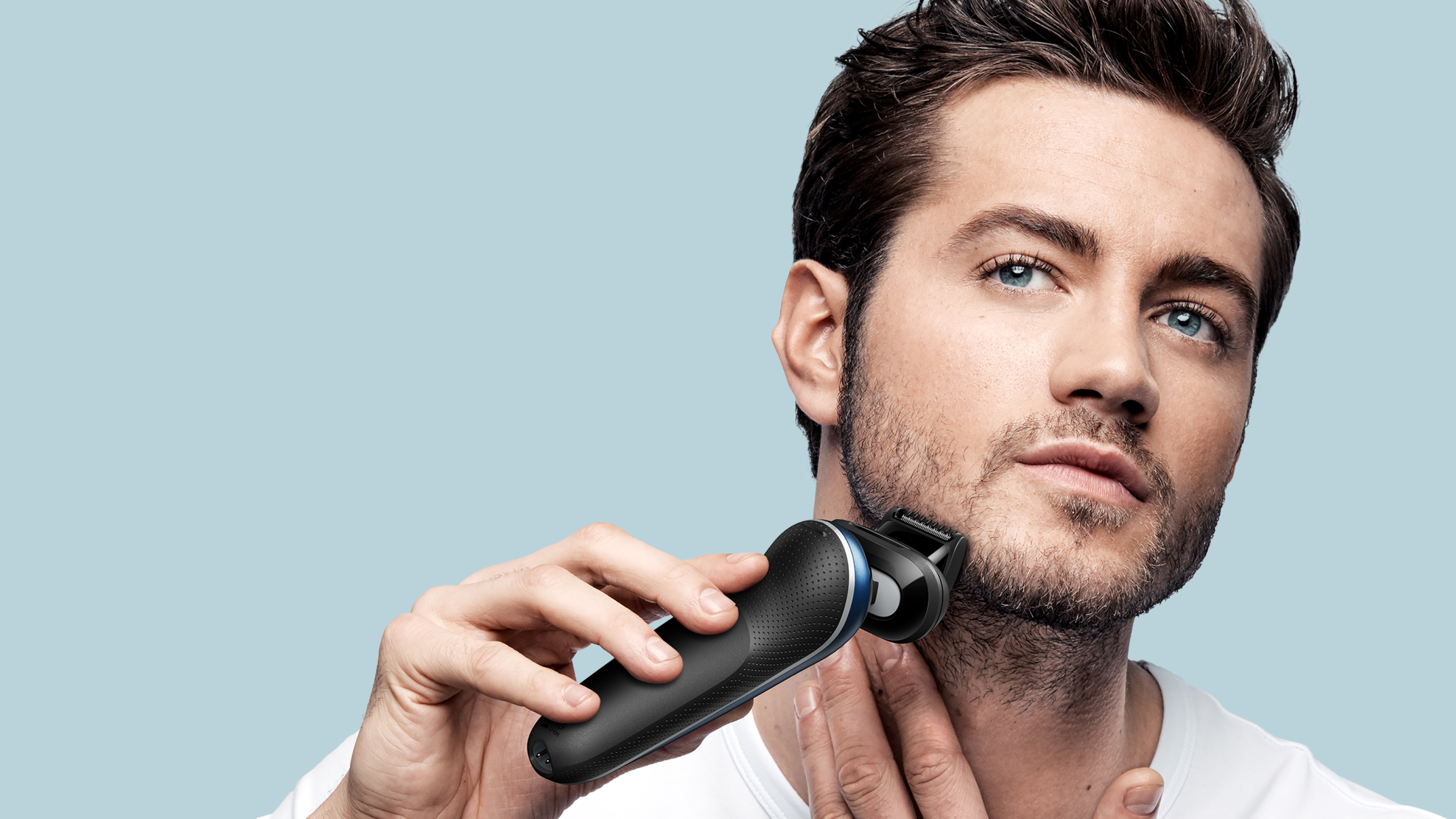 Man shaving his face, holding the device in one hand, placing his other hand on his neck for support