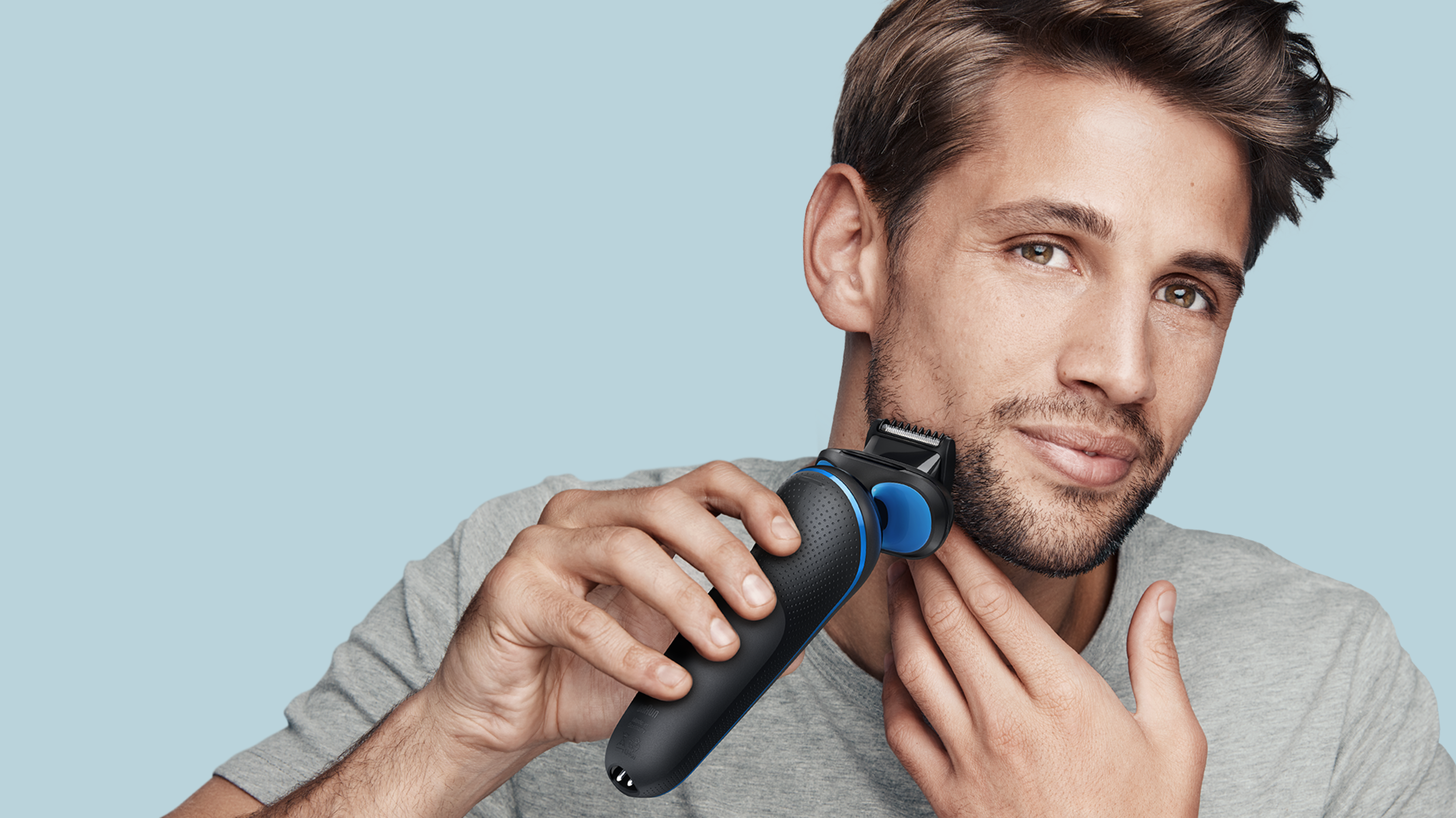 Man shaving his face, holding the device in one hand, placing his other hand on his neck for support