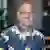 Headshot of Anthony Alosi with glasses and a gray beard wearing a navy blue floral Hawaiian shirt, posed indoors.
