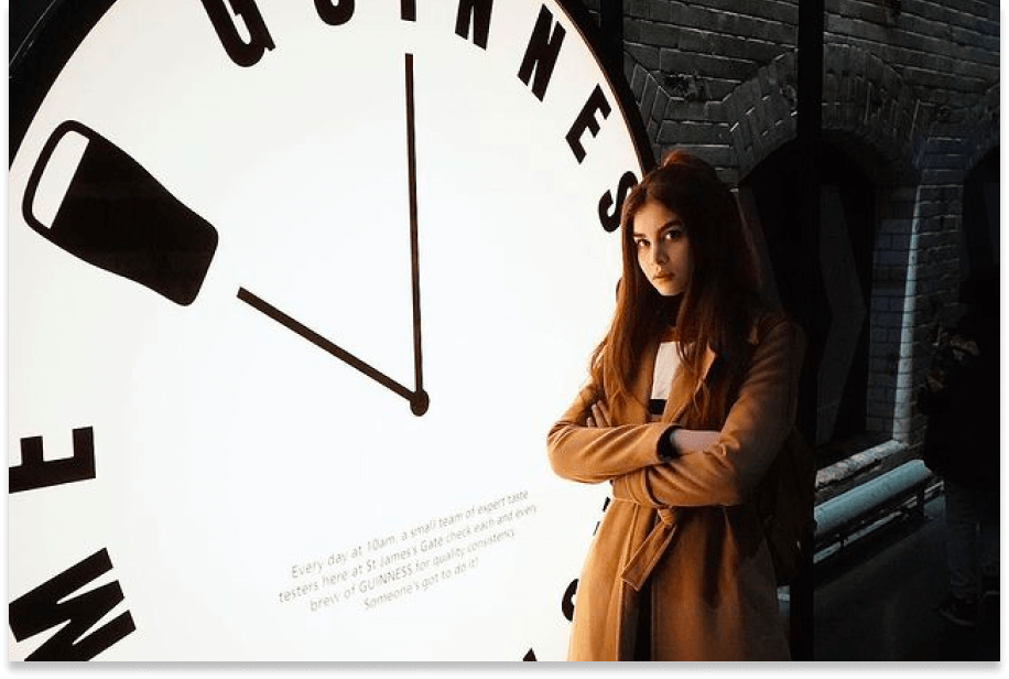 A girl standing  in front of the Guinness clock with her arms folded
