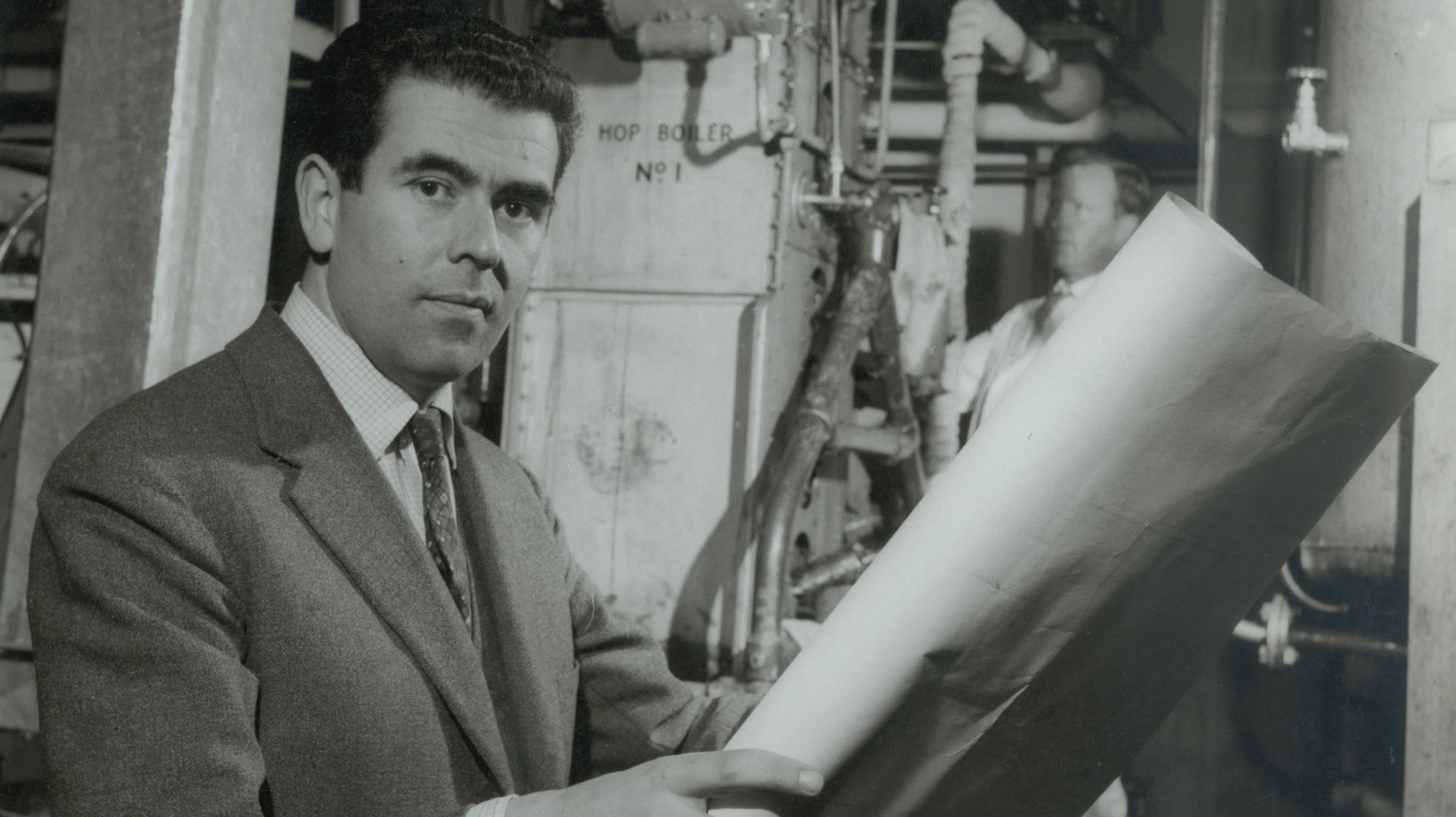 Michael Ash standing in front of a hop boiler, holding plans.
