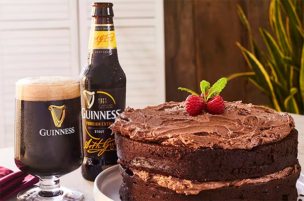 Guinness chocolate cake on a table next to a glass and bottle of Foreign Extra Stout