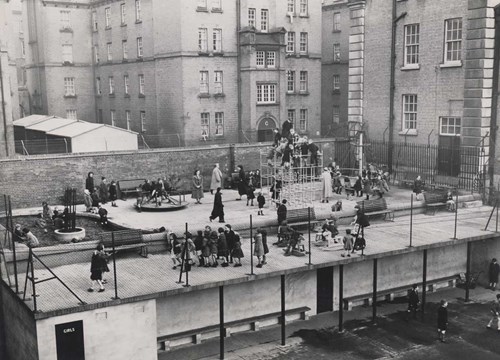Black and white photograph showing children playing in the outdoor playground to the rear of the Iveagh Play Centre, 1955.