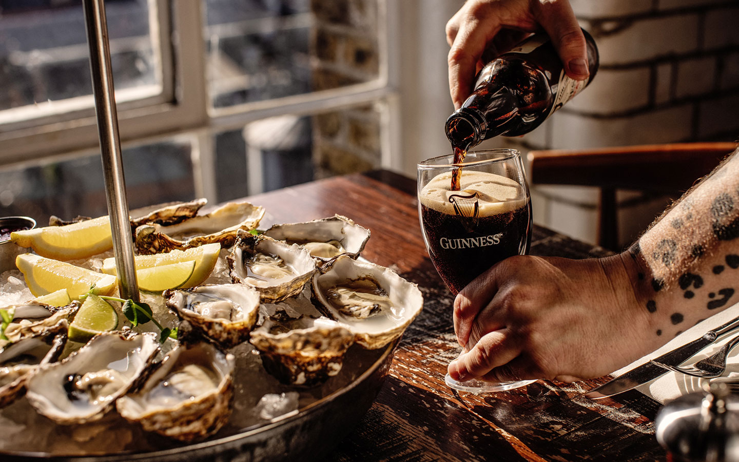 Group of friends laughing and enjoying their meal at the Brewers’ Dining Hall, one with the pairing of mussels & Guinness and another with hake & Hop House 13.