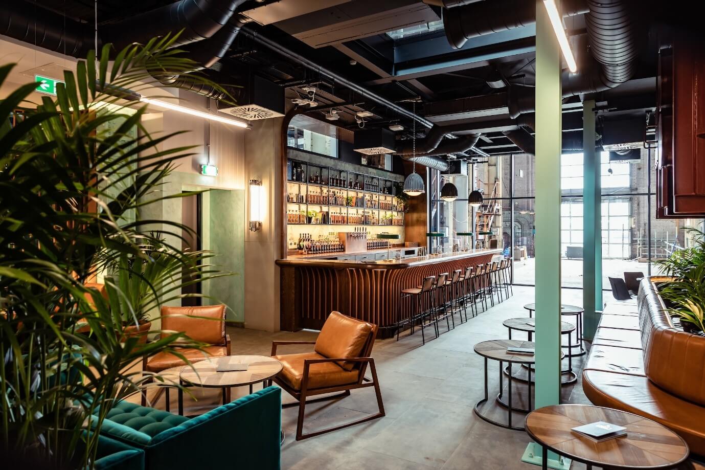 The powerhouse bar inside Roe & Co Distillery. The décor is leather with plants and lots of lighting, with a bar running along one side of the wall.
