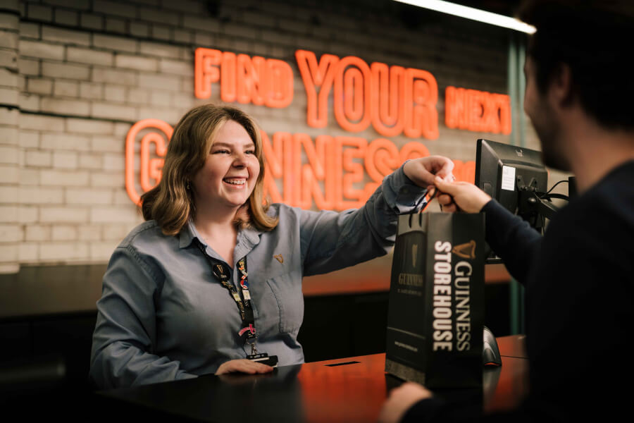 A smiling woman who works at Guinness Storehouse serving a customer at the retail counter