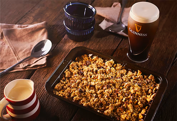 A crumble sitting on a wooden table with a pint of Guinness and a few spoons and napkins nearby