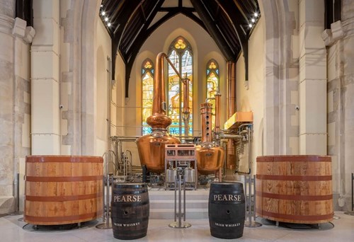 The inside of Pearse Lyon Distillery. Small and Large whiskey barrels can be seen with a large whiskey pot still in the back of the room.