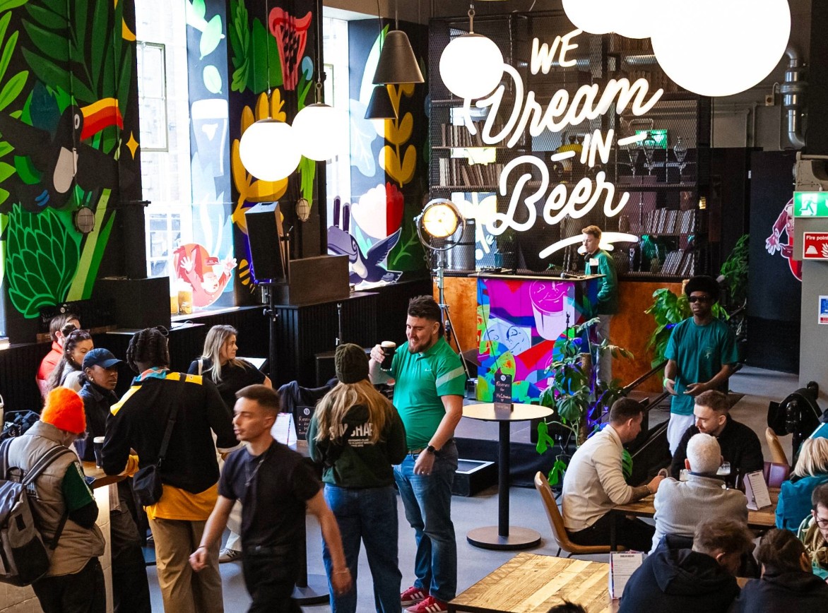 The inside area at Guinness Open Gate Brewery, with people at tables and standing drinking beers and water, with a DJ in the corner