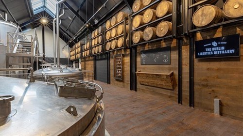 The inside of the Dublin Liberties Distillery. The walls are full of stacked barrels with large pot stills on whiskey on the opposite side.