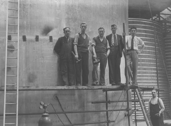 A group of workers pose for a picture on scaffolding in front of a large brewing tank