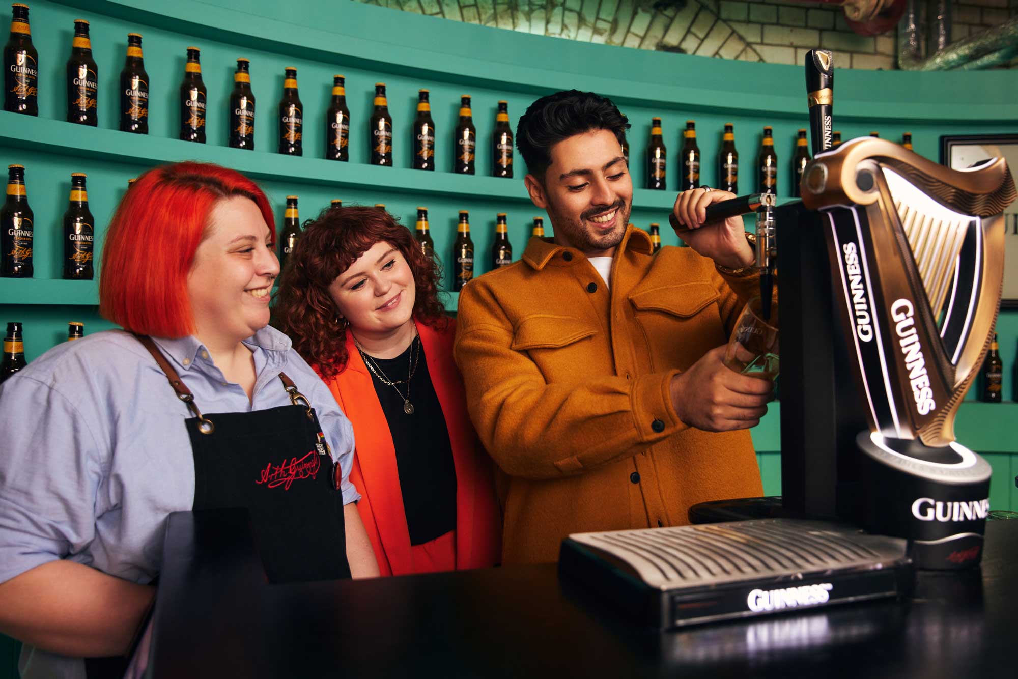 Two individuals behind the bar learning to pour their own pint of Guinness with one of our expert staff.