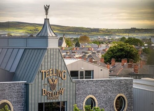 The Telling Whiskey Distillery with beautiful mountains and houses in the background. There is a rooster on top of the Teelings building.
