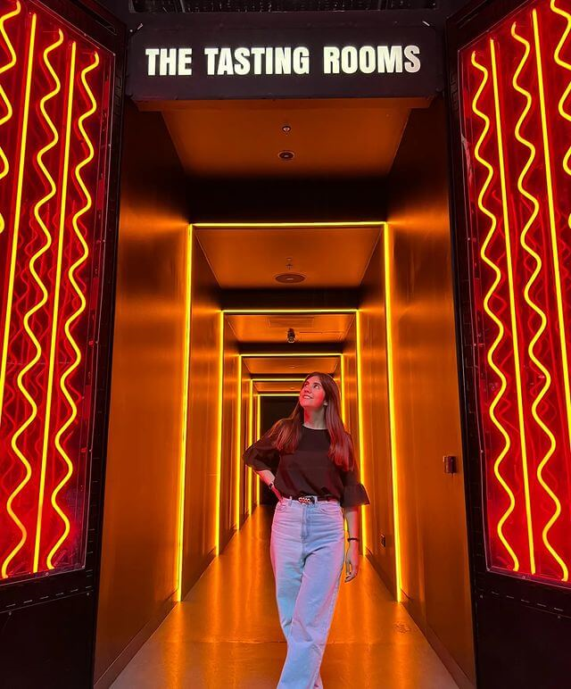 A girl happily standing in the entrance of the tasting room corridor with her hand on her hip looking up to the roof.
