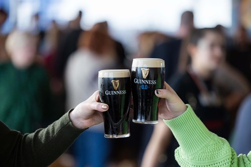 Two hands holding two pint of Guinness. One is the zero alcohol version, and the other the standard pint of Guinness.