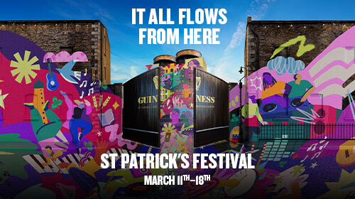 The Guinness Storehouse iconic black gates open showing the building and the gravity bar. Colourful illustrations are flowing outside the gates on to the walls representing the idea of it all flows from here