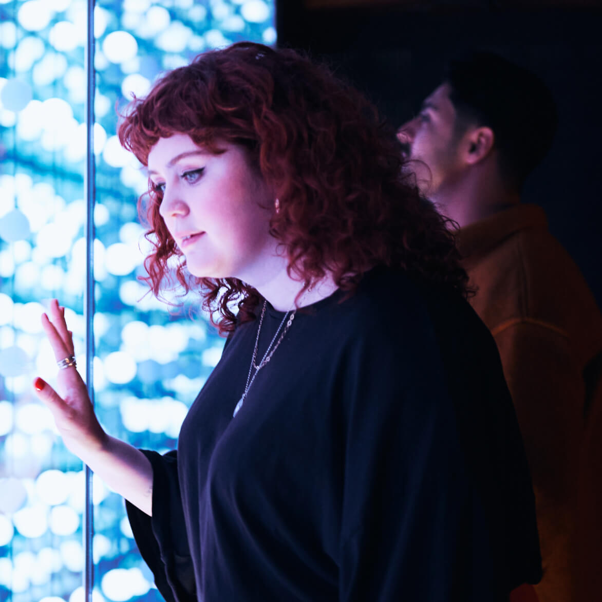 A girl gazing into the light wall within the Guinness Storehouse, there is a man in the background doing the same.