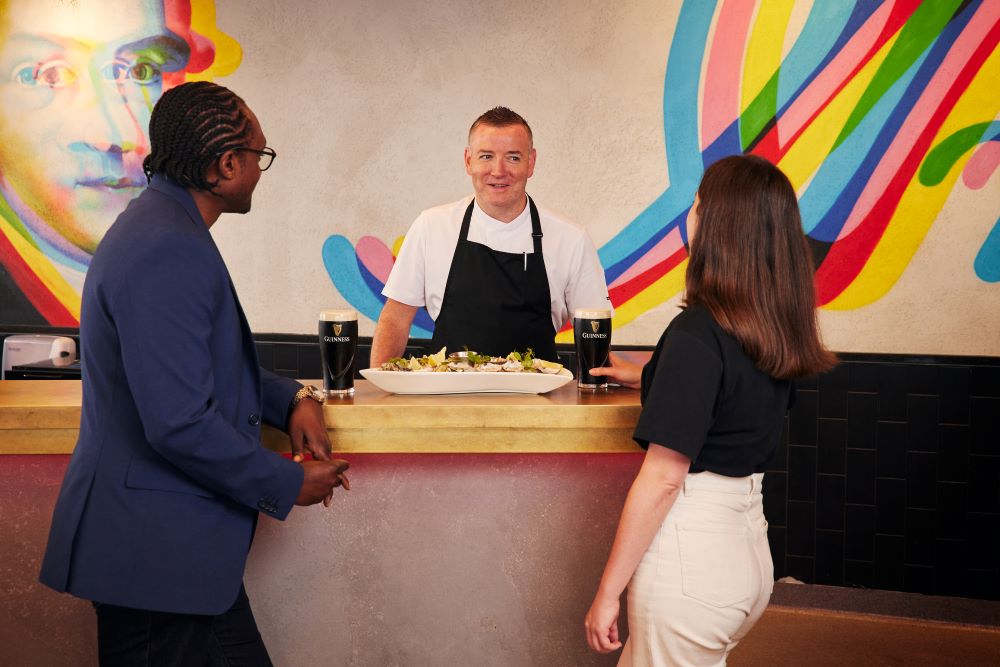 Two visitors enjoying Guinness and oysters on Gravity Bar while chat with the chef
