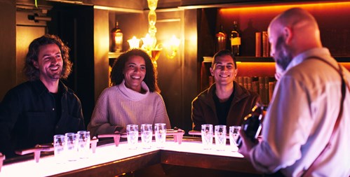 Three happy visitors at the bar listening to the tour guide during the Connoisseur Experience