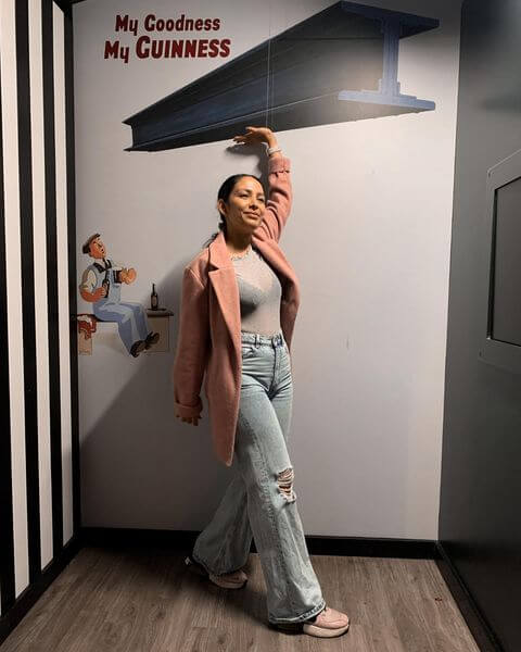 A girl standing in front of a wall with a Guinness image in the background. The girl is pretending to hold up a steel beam.