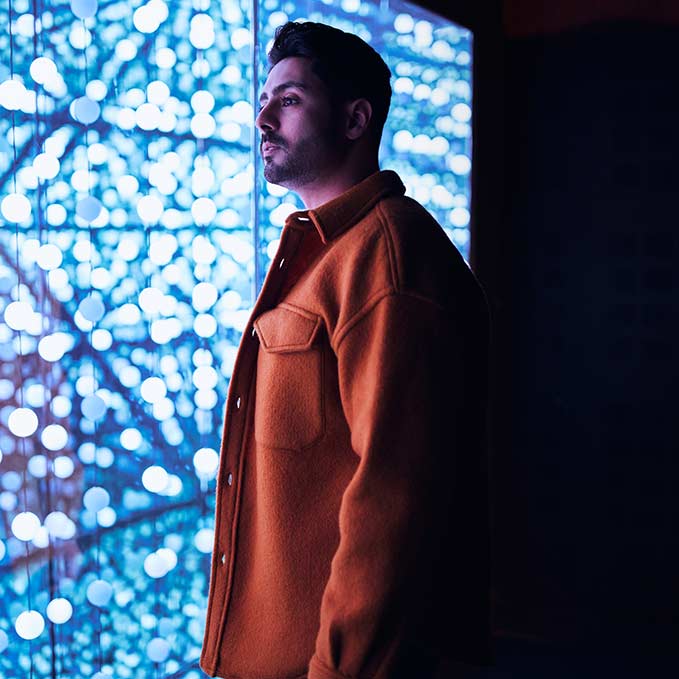 Man standing in front of light installation that looks like a wall of blue bubbles