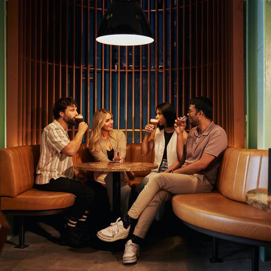 The Roe & Co Distillery building, large and red bricked and impressive, in front of a blue sky. A copper whiskey still is visible in the window