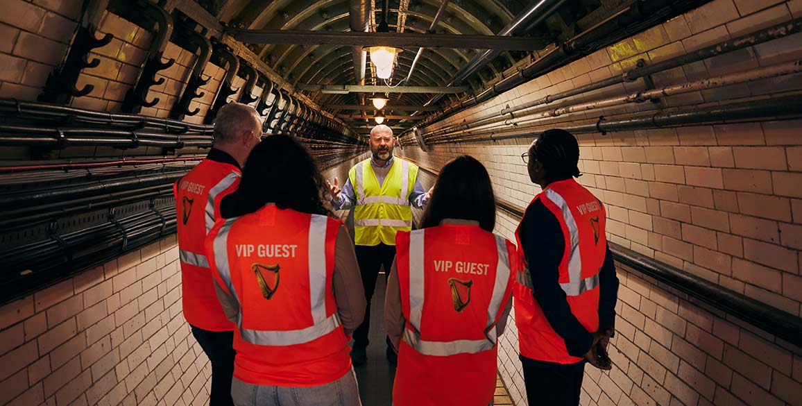 Four people in high vis vests stand in a tunnel listening to a tour guide speak